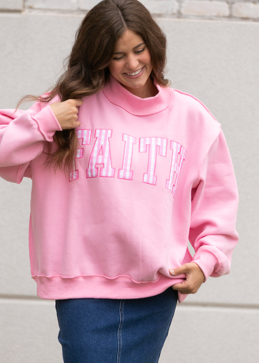 Bright pink oversized sweatshirt with gingham Faith lettering, mockneck, and relaxed fit.