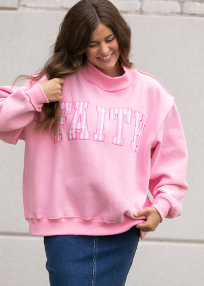Bright pink oversized sweatshirt with gingham Faith lettering, mockneck, and relaxed fit.