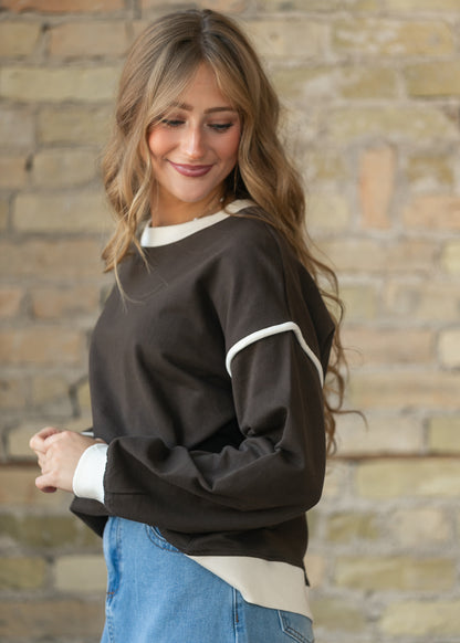 Side view of espresso crewneck sweater showing oversized fit and cream contrast sleeve trim.