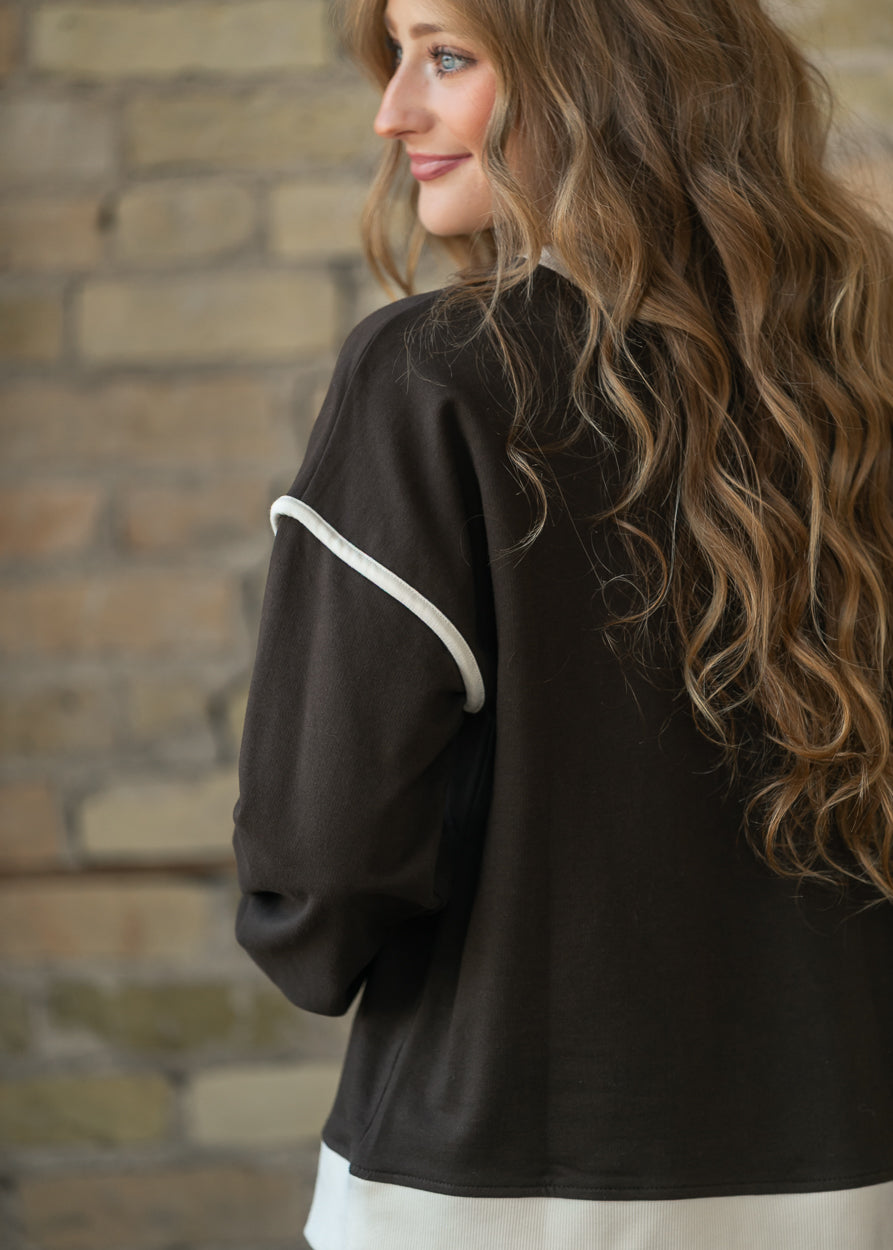 Close-up of espresso sweater showing cream contrast trim along the dropped shoulder seam.