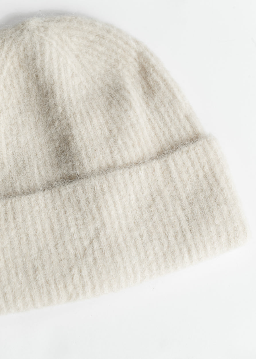 Close-up of soft ivory ribbed beanie showing fuzzy knit texture and folded cuff.