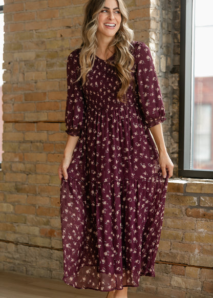 Burgundy floral midi dress with smocked bodice, three-quarter puff sleeves, and tiered skirt.