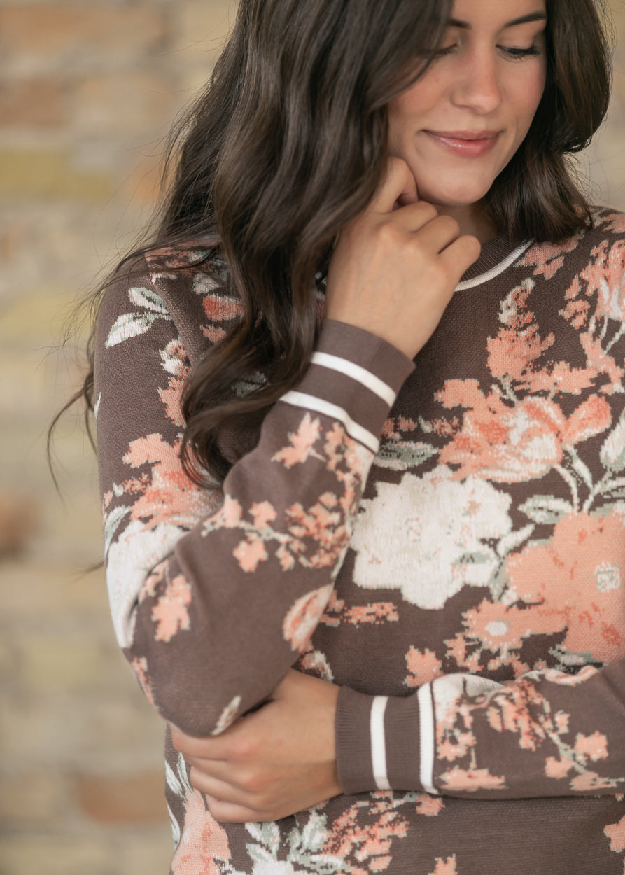 Close-up of brown floral jacquard sweater showing peach florals and striped cuff detail.