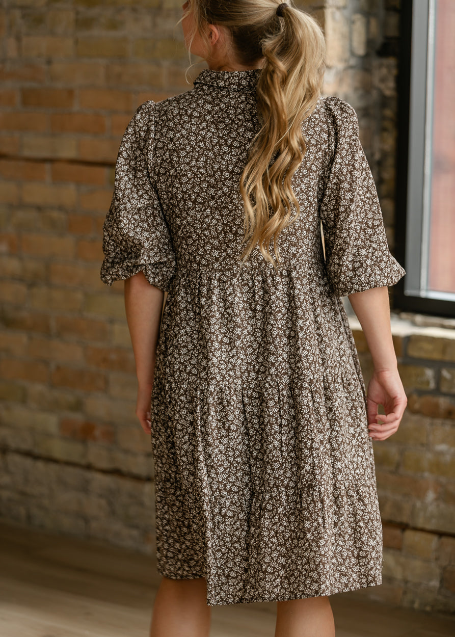 Back of brown floral button-up dress showing gathered waist, puff sleeves, and knee-length hem.