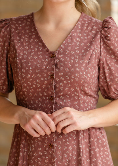 Close-up of brown floral midi dress showing V-neckline, petite print, buttons, and puff sleeves.