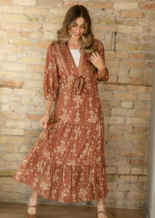 Rust brown floral V-neck midi dress layered over a white top, with the tiered skirt held out to show its fullness.