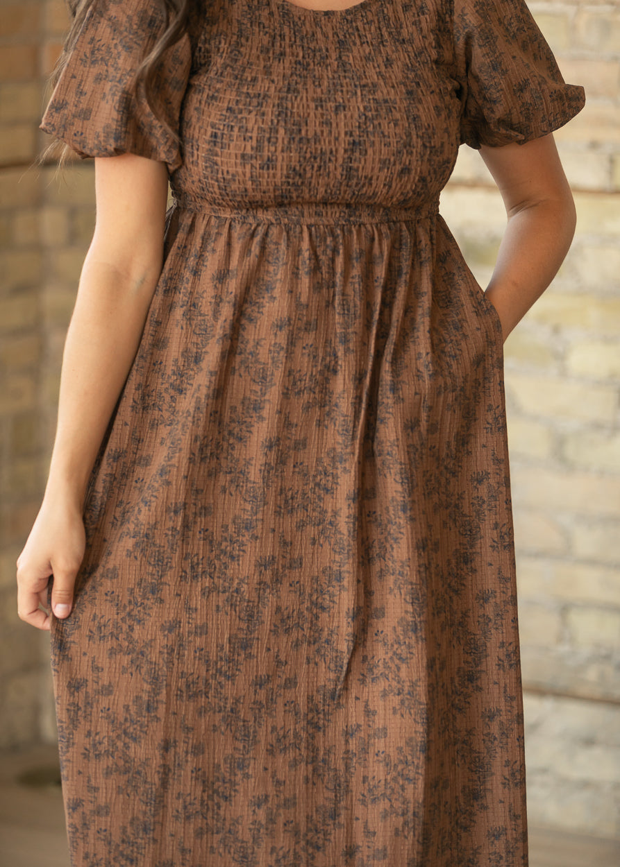 Close-up of brown floral midi dress showing smocked bodice, gathered waist, and side pocket.