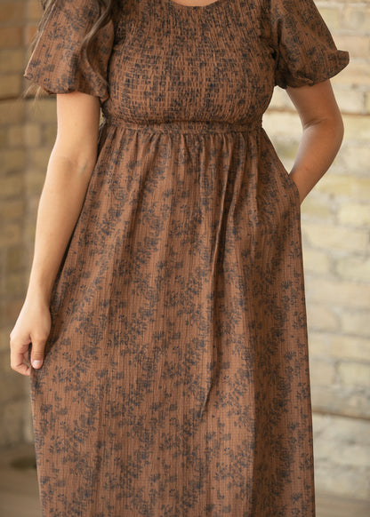 Close-up of brown floral midi dress showing smocked bodice, gathered waist, and side pocket.