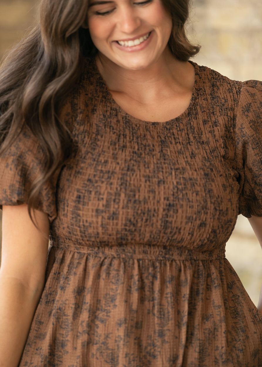 Close-up of brown floral midi dress showing rounded neckline, smocked bodice, and puff sleeves.