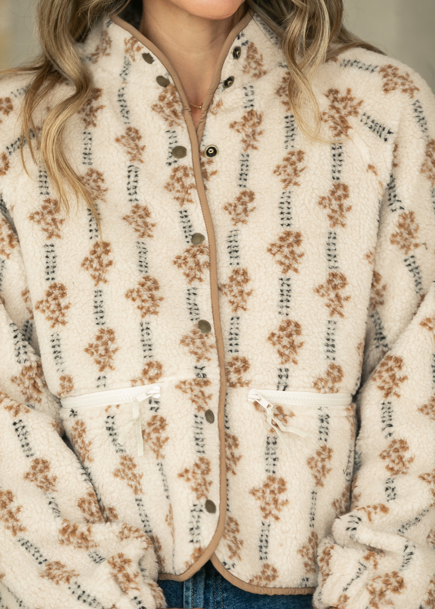Close-up of cream floral fleece jacket showing snap front, contrast binding, and functional zip pockets.