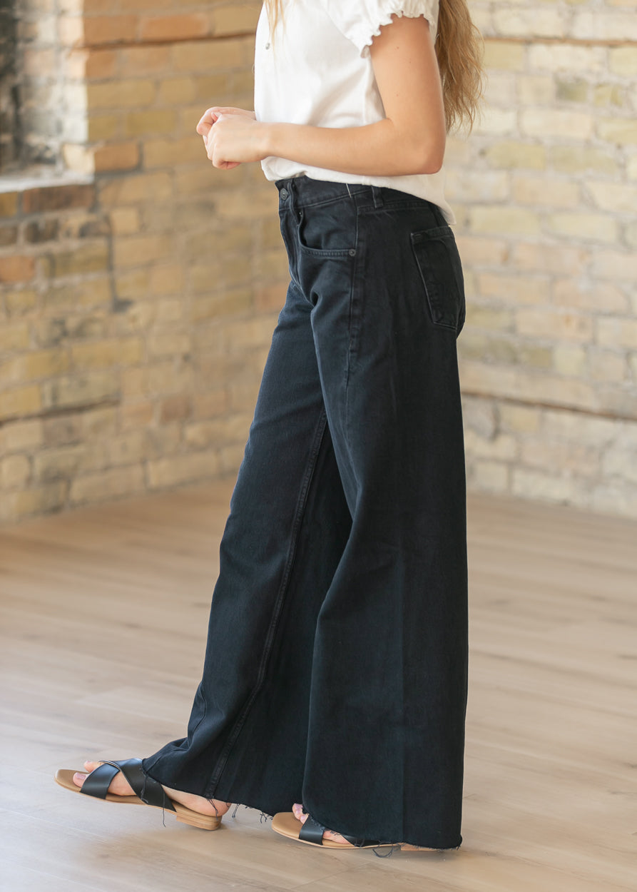Side view of black wide leg boyfriend jeans with raw hem and high rise waist