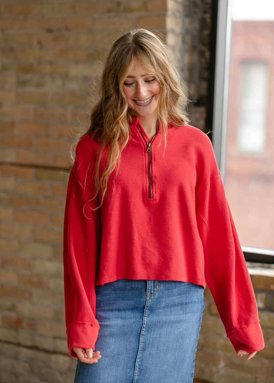 Close-up of red Celeste quarter-zip top showing functional zipper, ribbed texture, and stand collar.
