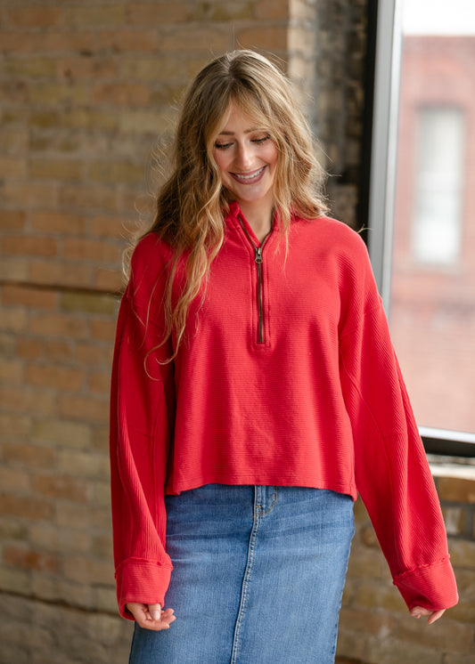 Close-up of red Celeste quarter-zip top showing functional zipper, ribbed texture, and stand collar.