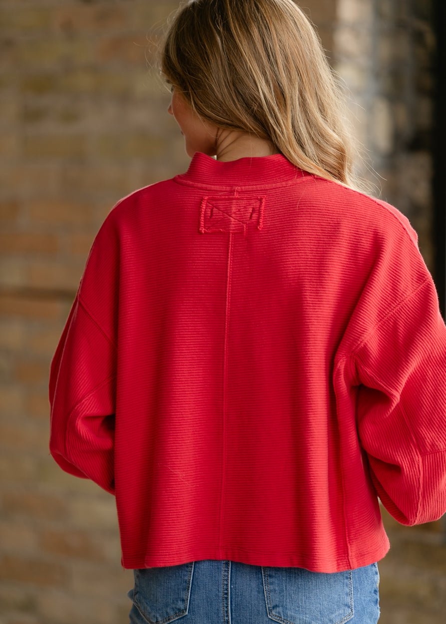 Back detail of bright red quarter-zip top with raw-edge seam construction and ribbed texture.
