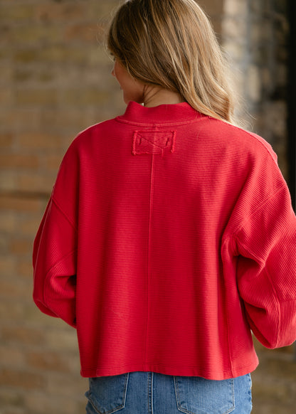 Back detail of bright red quarter-zip top with raw-edge seam construction and ribbed texture.