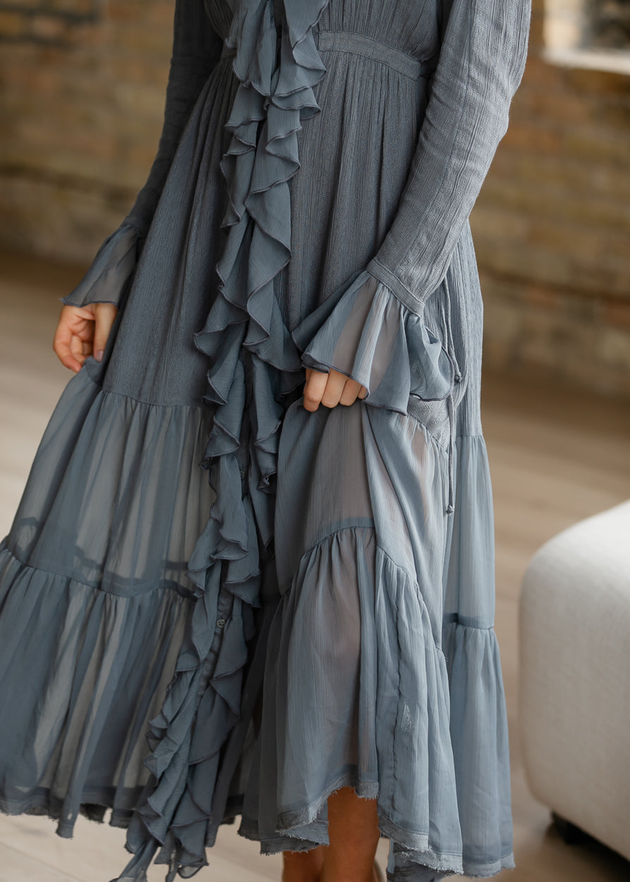 Close-up of slate blue-grey midi dress showing flared ruffle cuffs, cascading trim, and sheer tiered skirt panels.