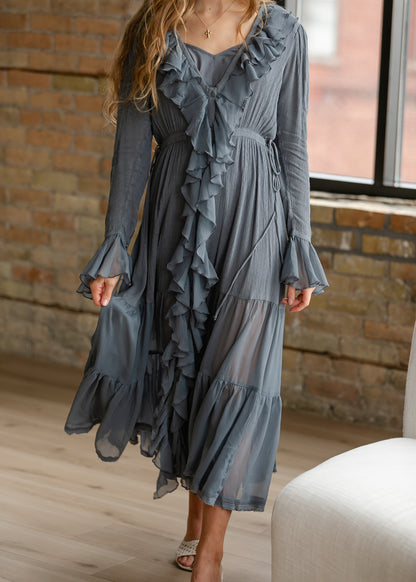 Slate blue-grey ruffle midi dress styled with neutral heels, showing the flowing tiered skirt and long sleeves.