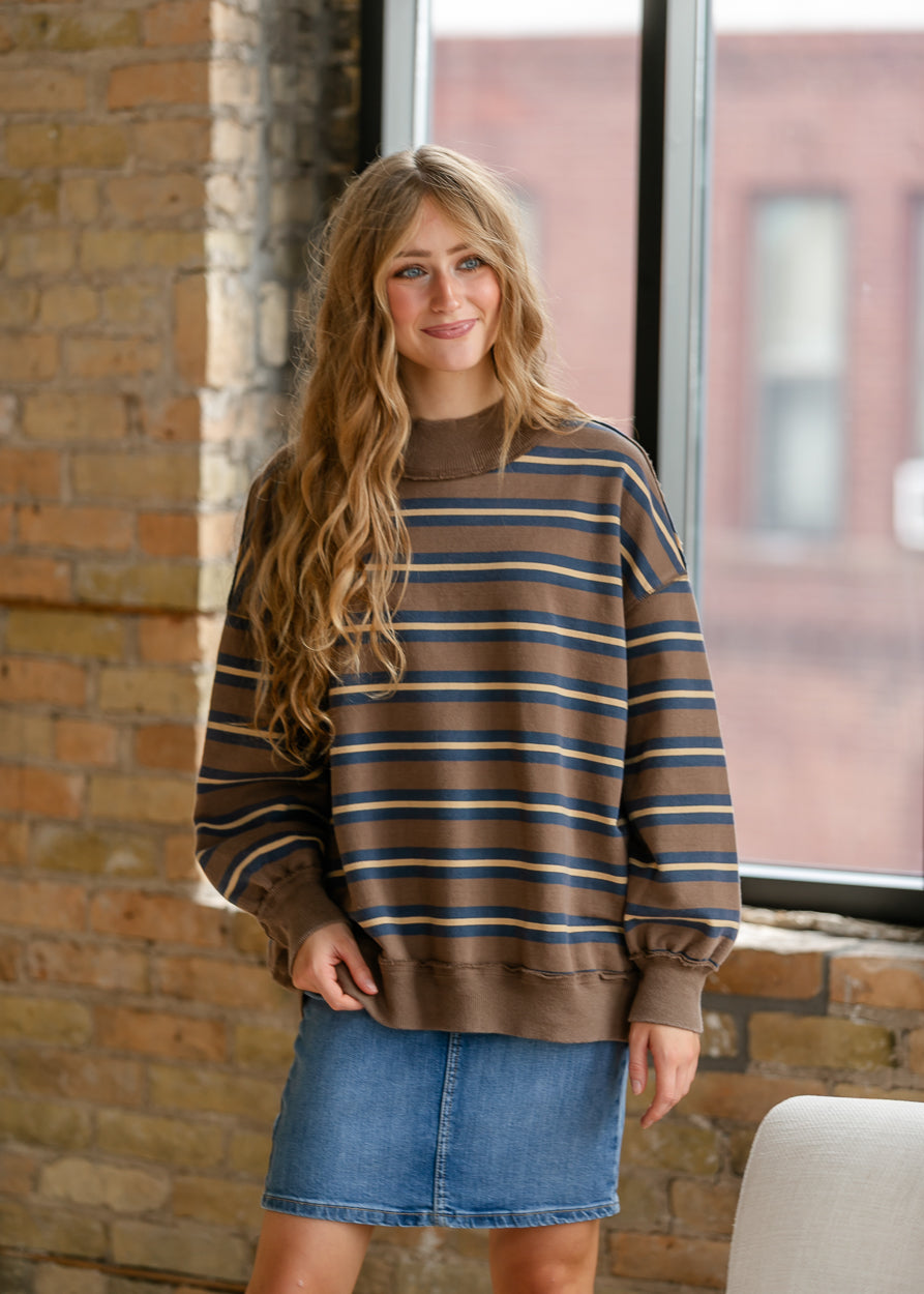 Full-length styling of oversized Free People striped top with denim skirt and neutral sneakers.