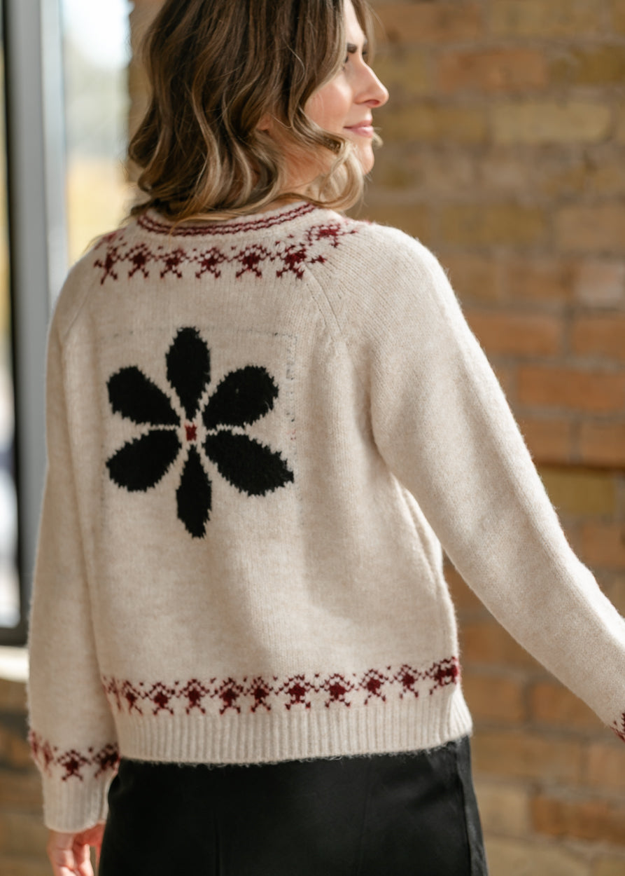 Back of ivory floral cardigan showing large black flower motif and red geometric knit detail.