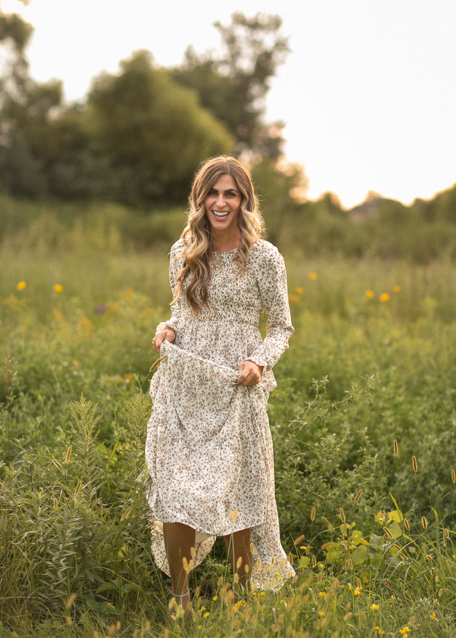 Gia ivory floral maxi dress with smocked bodice, long sleeves, and tiered skirt in a sunlit meadow.