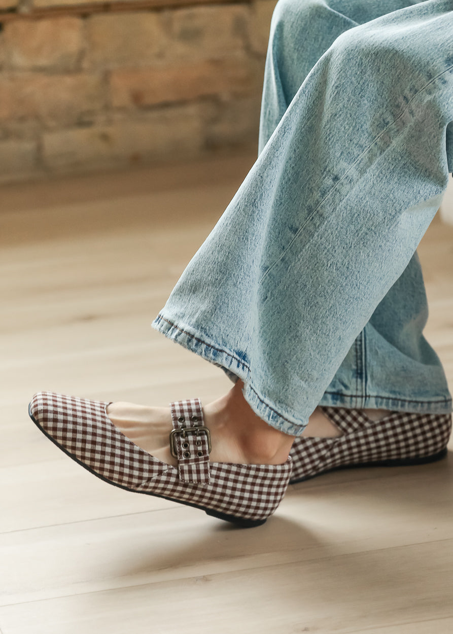 Brown gingham Mary Jane ballet flats with low heel and metal buckle, worn with wide-leg denim.