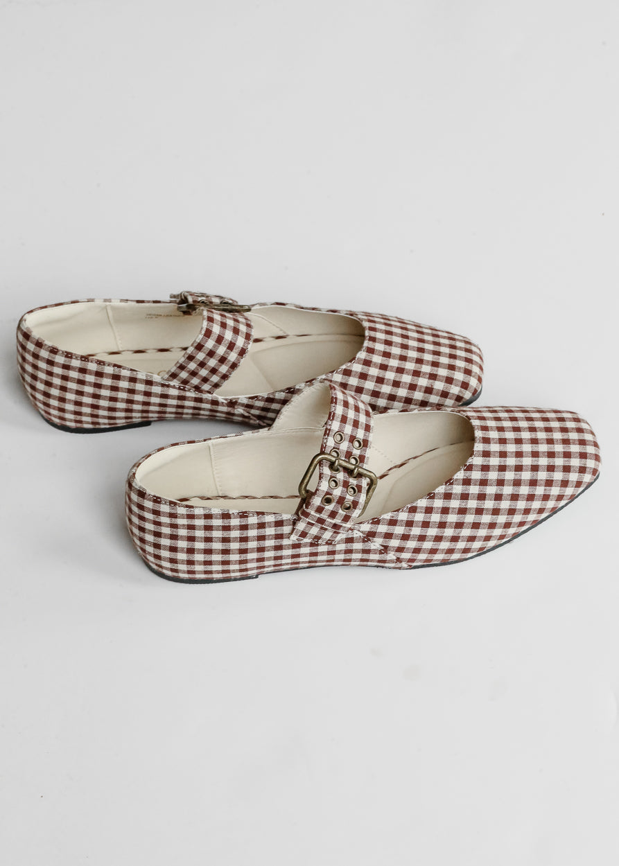 Brown gingham ballet flats with adjustable buckle strap and low heel on white background.