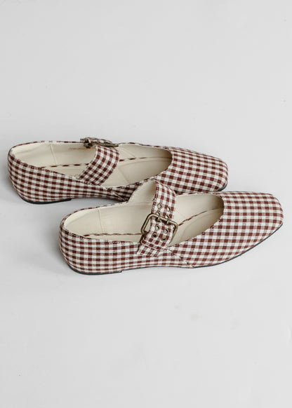 Brown gingham ballet flats with adjustable buckle strap and low heel on white background.