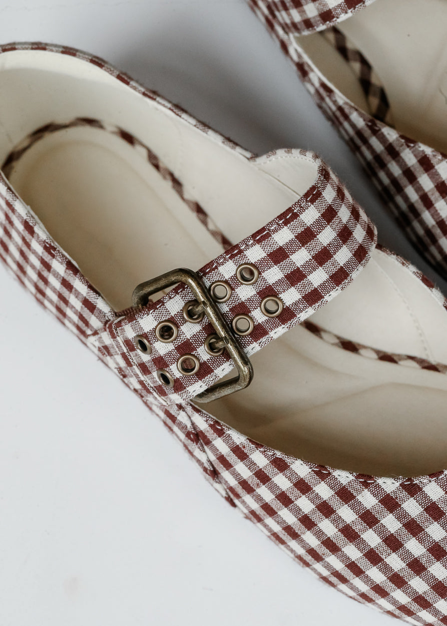 Close-up of adjustable buckle strap with metal grommet detailing on brown gingham ballet flat.