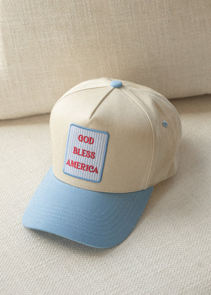 Close-up of cream trucker hat with sky-blue curved brim and GOD BLESS AMERICA embroidered patch