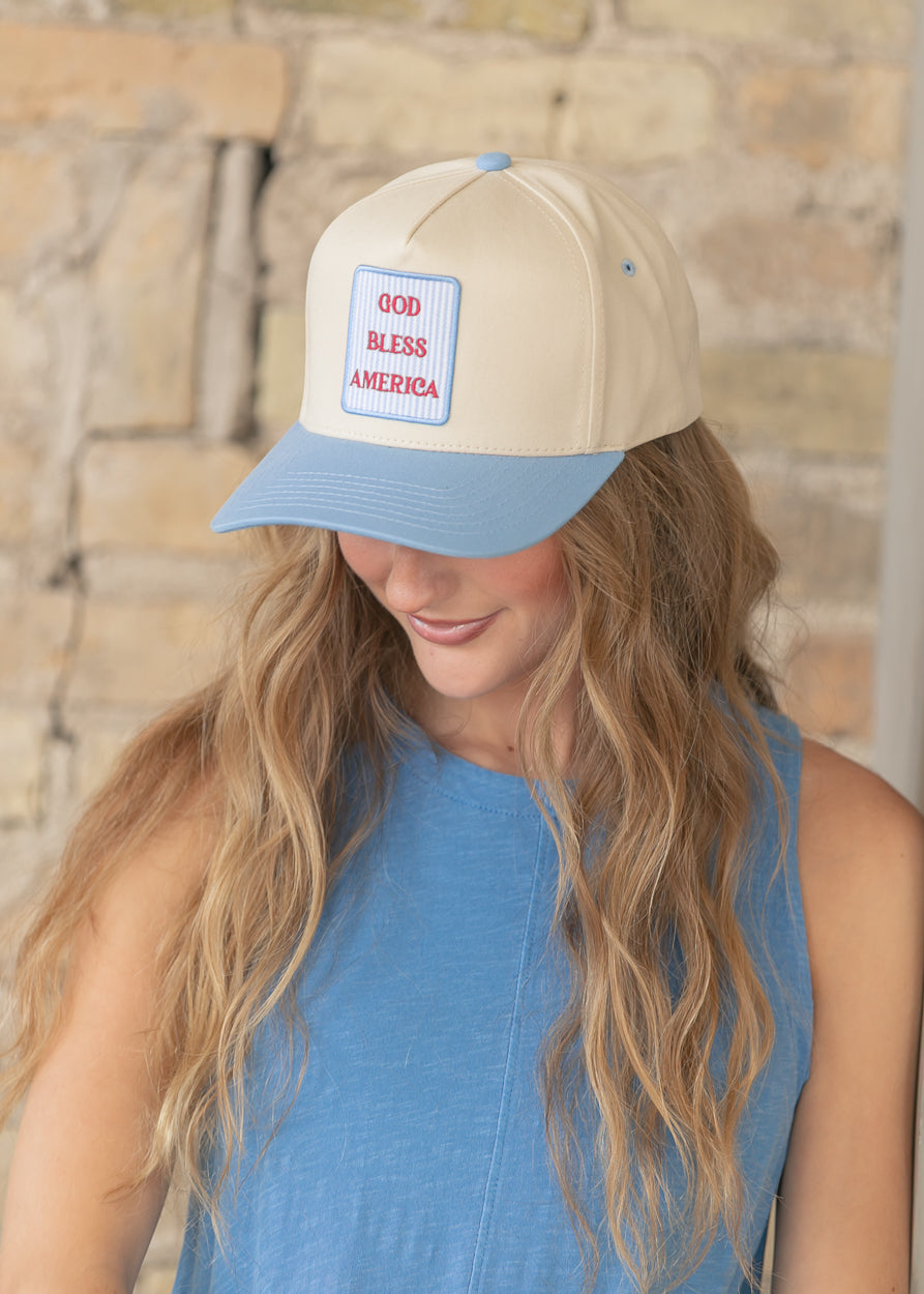 Close-up of cream trucker hat with sky-blue curved brim and GOD BLESS AMERICA embroidered patch