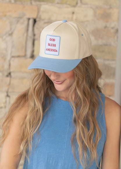 Close-up of cream trucker hat with sky-blue curved brim and GOD BLESS AMERICA embroidered patch