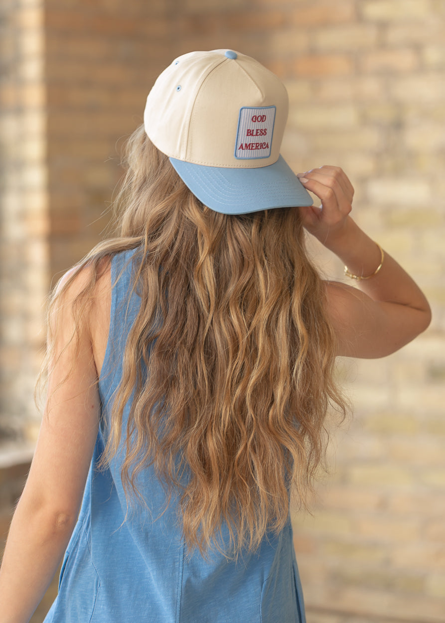Cream and blue trucker hat with red GOD BLESS AMERICA embroidered patch, worn with a blue sleeveless dress