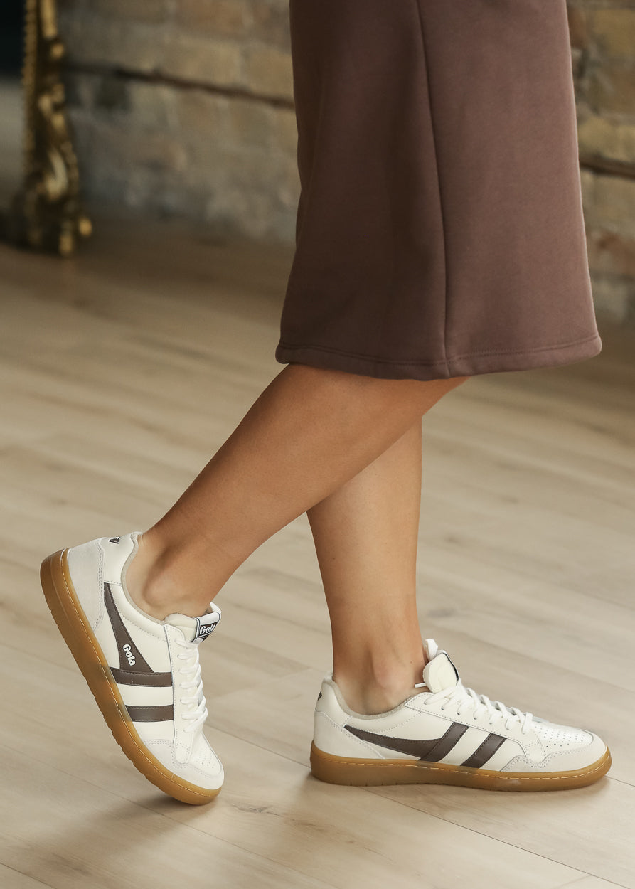 Ivory Gola Eagle '86 sneakers with brown side stripes and gum soles, worn with a brown skirt.