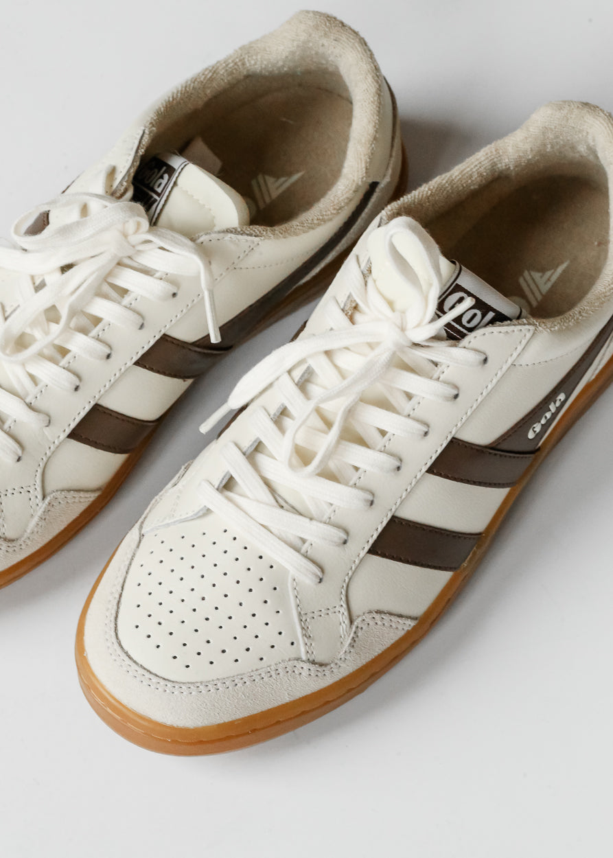 Close-up of ivory Gola Eagle '86 sneakers showing brown stripes, perforated toe detail, and gum sole.