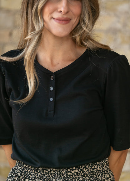 Close-up of black Grace cotton shirt showing V-neckline, puff shoulder, and functional three-button placket.