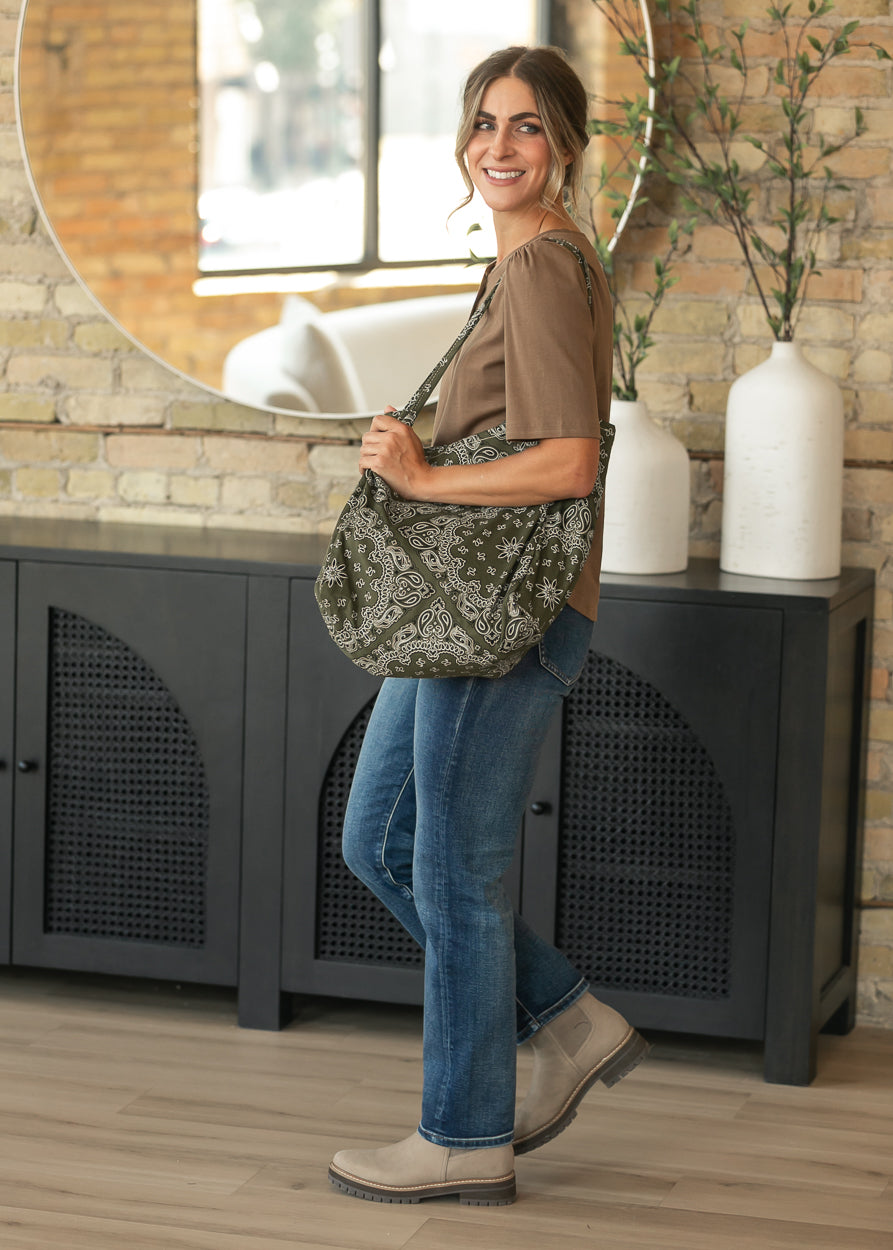 Dark wash slim jeans styled with a brown top, taupe boots, and an olive bandana print tote.