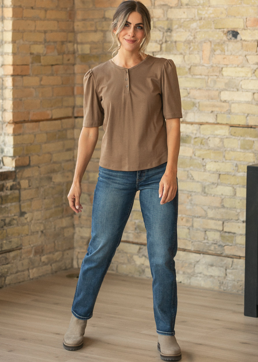 Dark wash slim jeans styled with a brown puff sleeve top and taupe ankle boots.