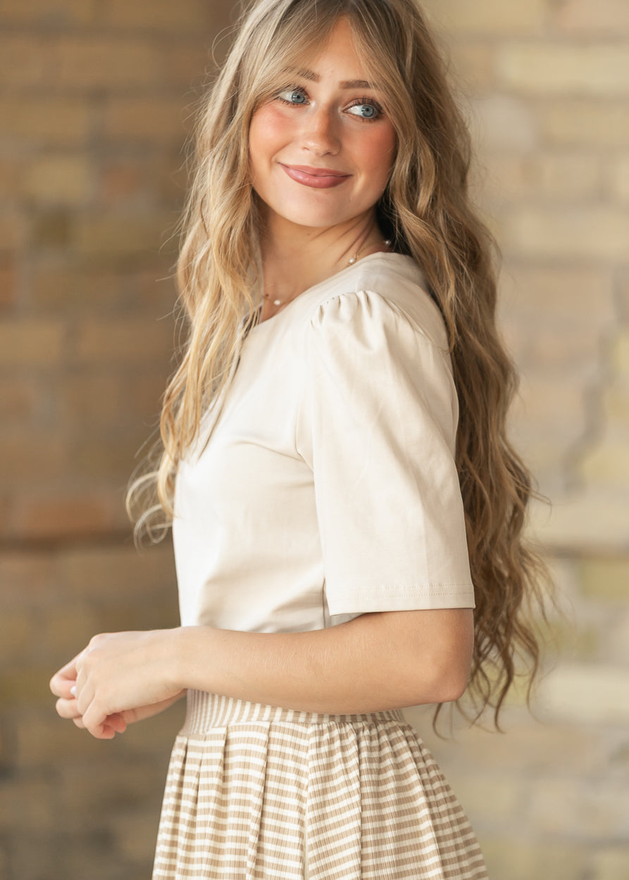 Side view of cream Grace top with puff shoulder and elbow-length sleeve, styled with a striped skirt.