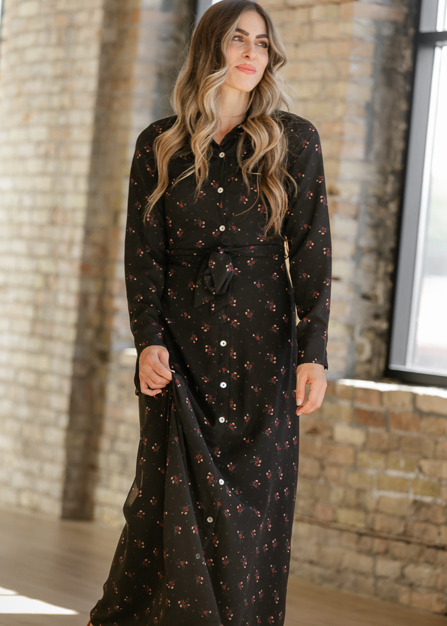 Black maxi dress with scattered red and pink florals, shown with the skirt held out to display its shape.