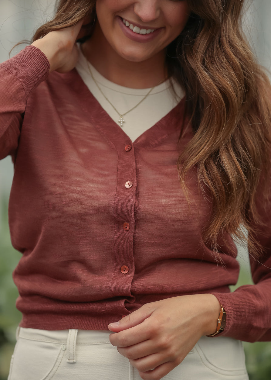 Close-up of rust sheer knit cardigan with v neckline and tonal buttons
