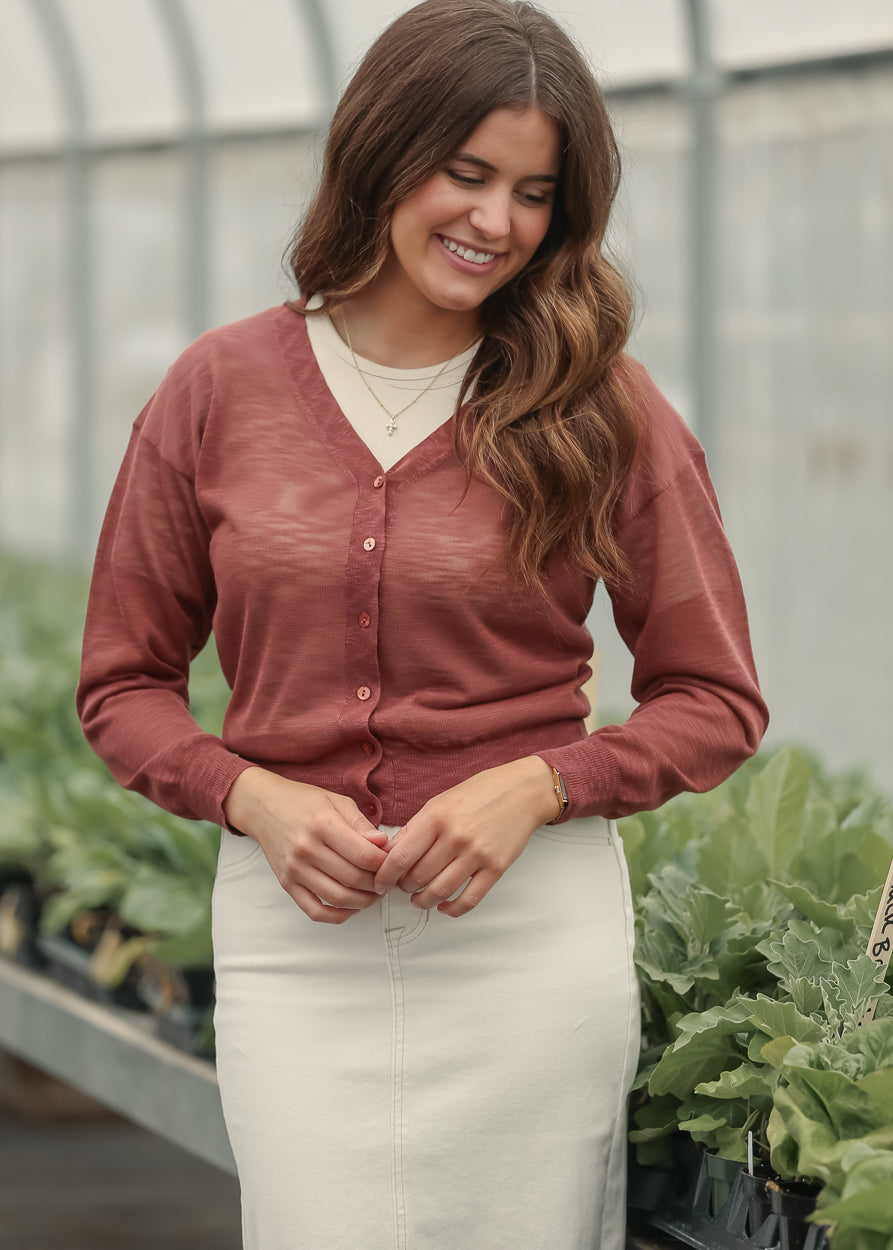 Rust lightweight v neck cardigan layered over a cream denim maxi skirt in a greenhouse