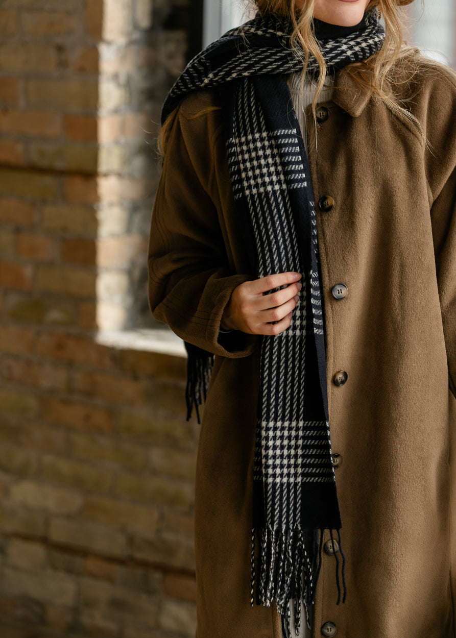 Black and white plaid scarf with houndstooth accents and fringe trim, styled over a brown coat.