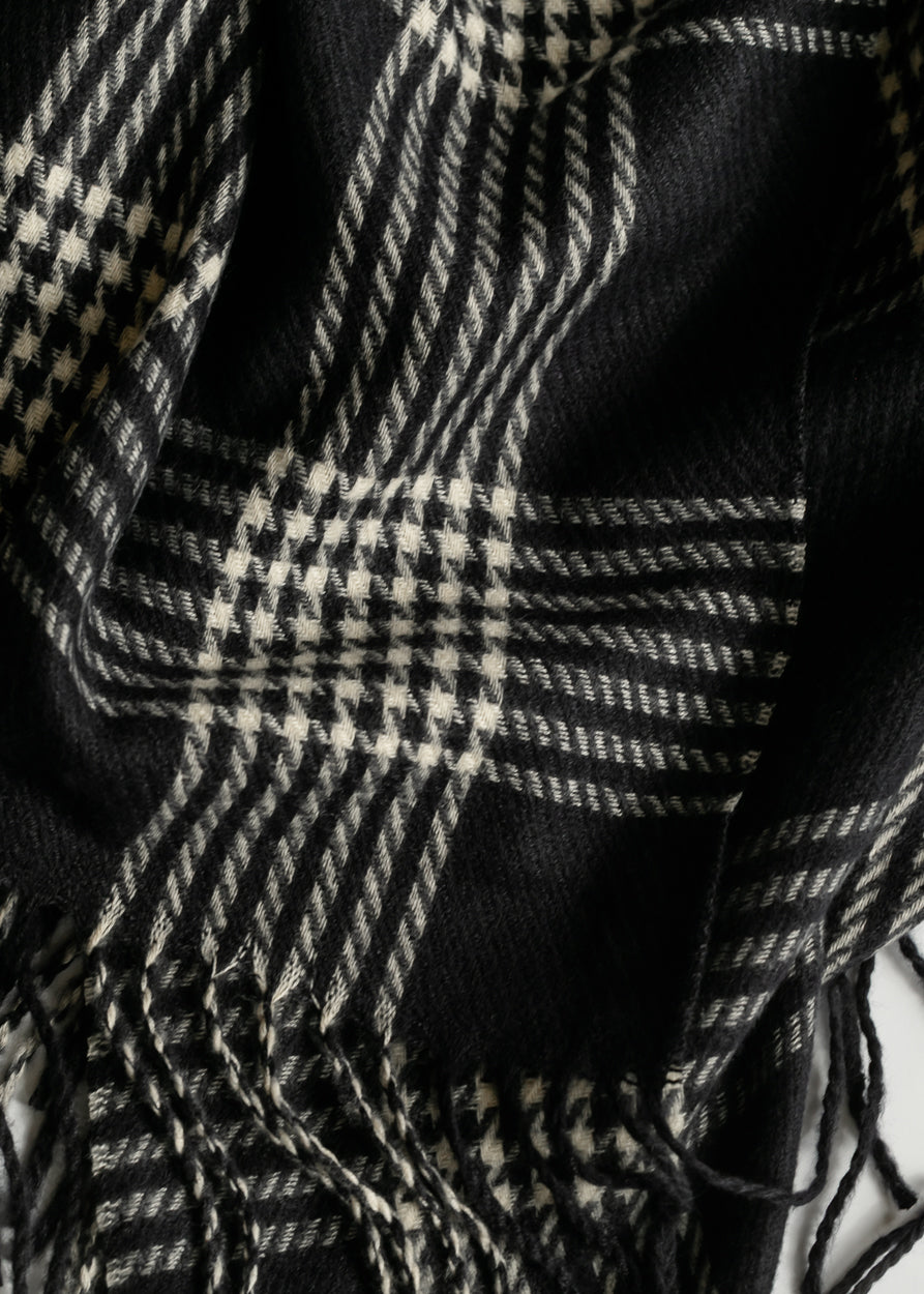 Close-up of black and white woven scarf showing mixed plaid and houndstooth patterns with fringe.