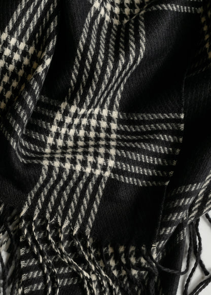 Close-up of black and white woven scarf showing mixed plaid and houndstooth patterns with fringe.