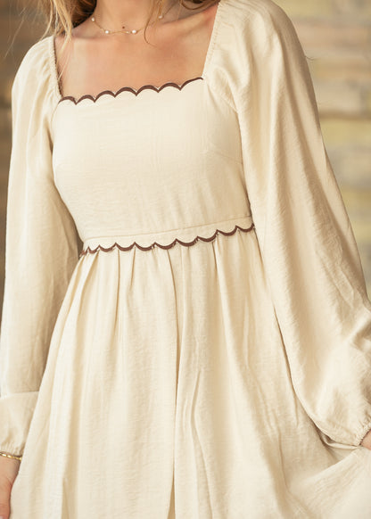 Close-up of cream square neck dress with chocolate brown scalloped trim and gathered skirt.