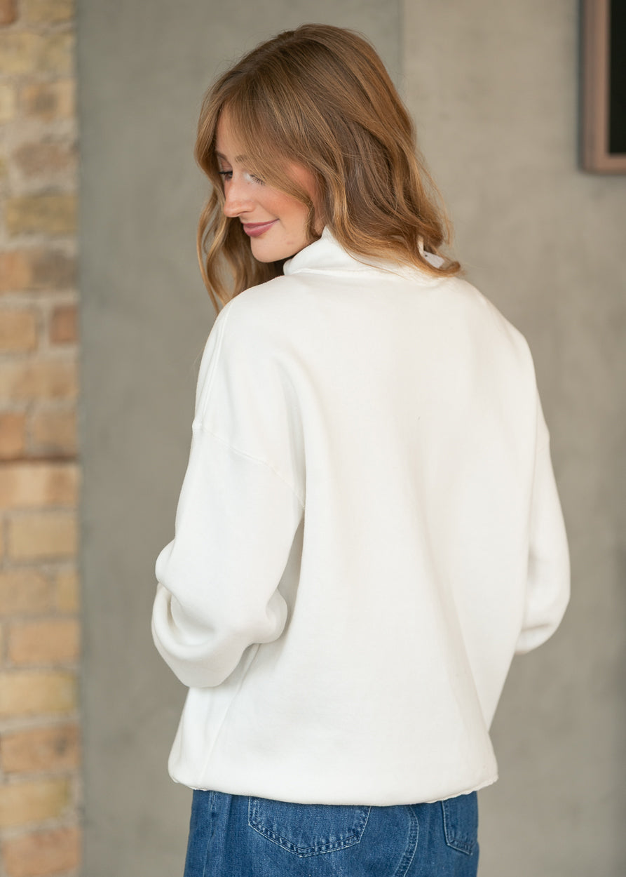 Back of cream mockneck sweatshirt showing the loose fit, drop shoulders, and hip-length silhouette.