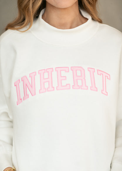 Close-up of cream sweatshirt showing the mockneck and pink Inherit lettering across the chest.