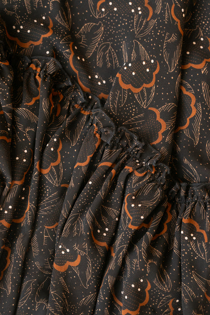 Close-up of black floral leaf print with warm brown accents and gathered tiered seam.