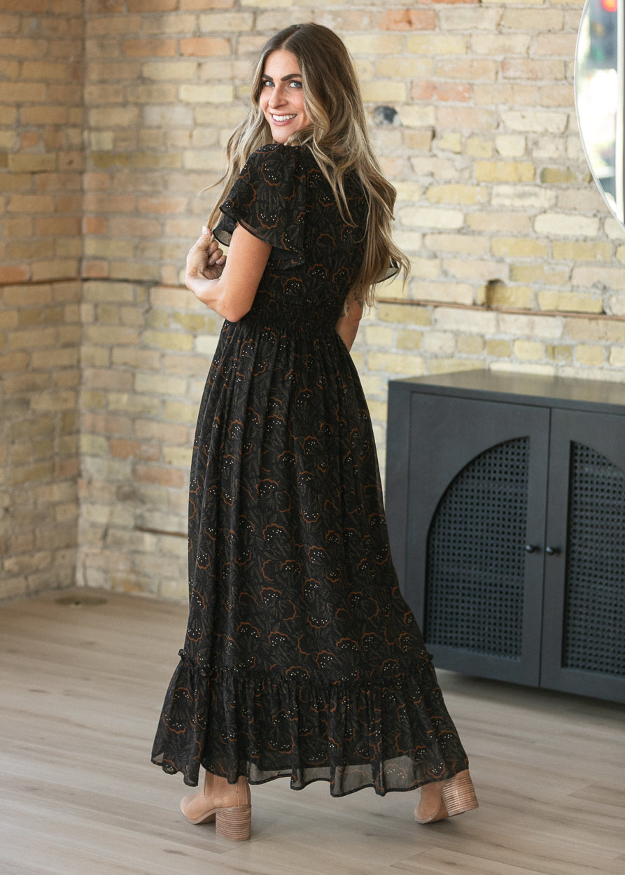 Black floral leaf maxi dress with smocked waist and flowing ankle-length skirt, shown from the back.