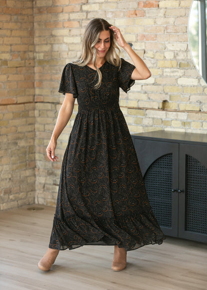 Black floral leaf maxi dress with modest V-neck, flutter sleeves, smocked waist, and tiered hem.